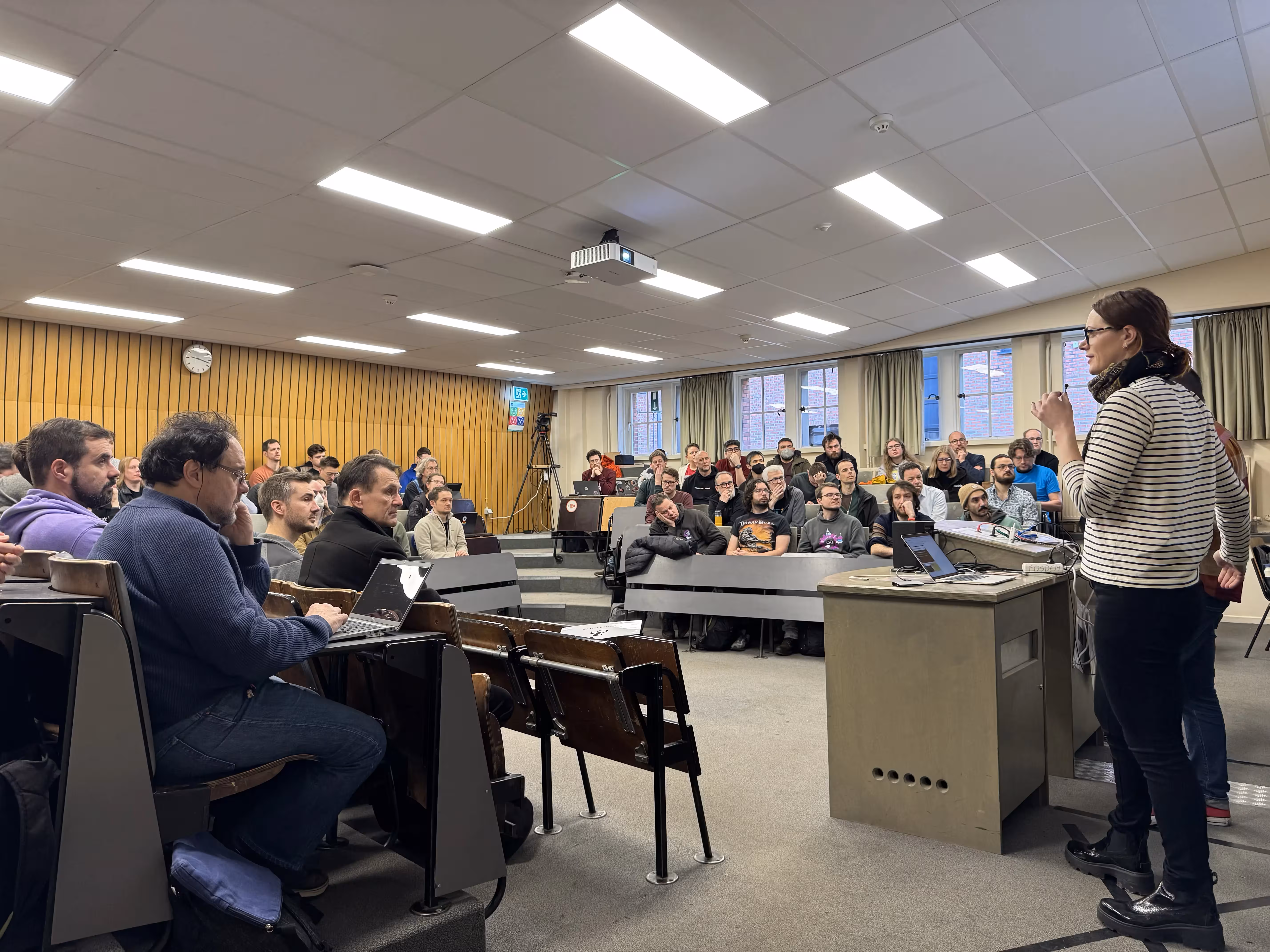 A picture of a lecture room that is full, while two speakers give a talk.